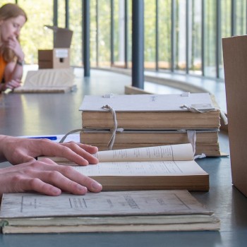 Studiezaal van het IISG waarin op een tafel twee handen de pagina's van een oud boek doorbladeren.