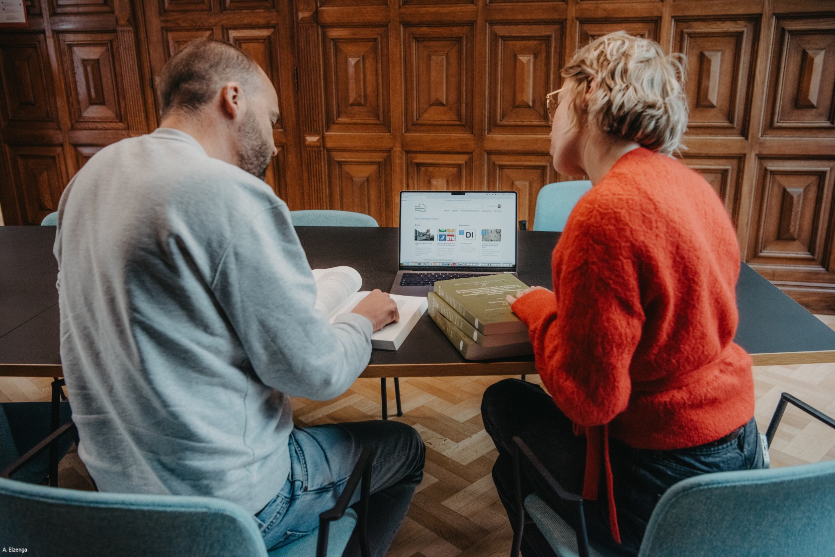 Een man en een vrouw zitten aan een bureau en kijken naar een laptop.